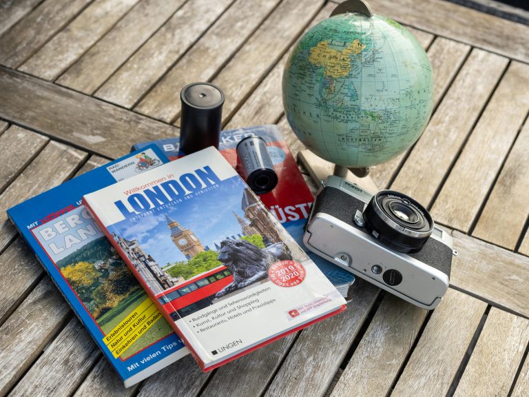 Travel guides, globe and vintage camera on a wooden table for summer 2026 trip planning